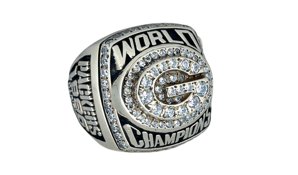 A silver championship ring adorned with diamonds, featuring a prominent letter "G" in the center. The words "World Champions" are engraved on the top and bottom. The sides display additional engravings and designs.