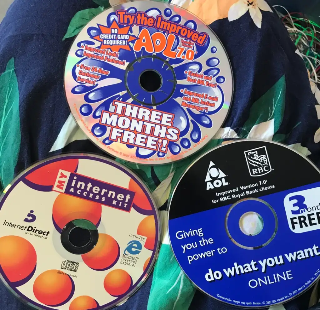 Three colorful CDs are displayed on a floral fabric. The top CD offers AOL 7.0 with three months free. The bottom left features an Internet Access Kit, and the bottom right is a CD for AOL/RBC clients, also offering three months free.