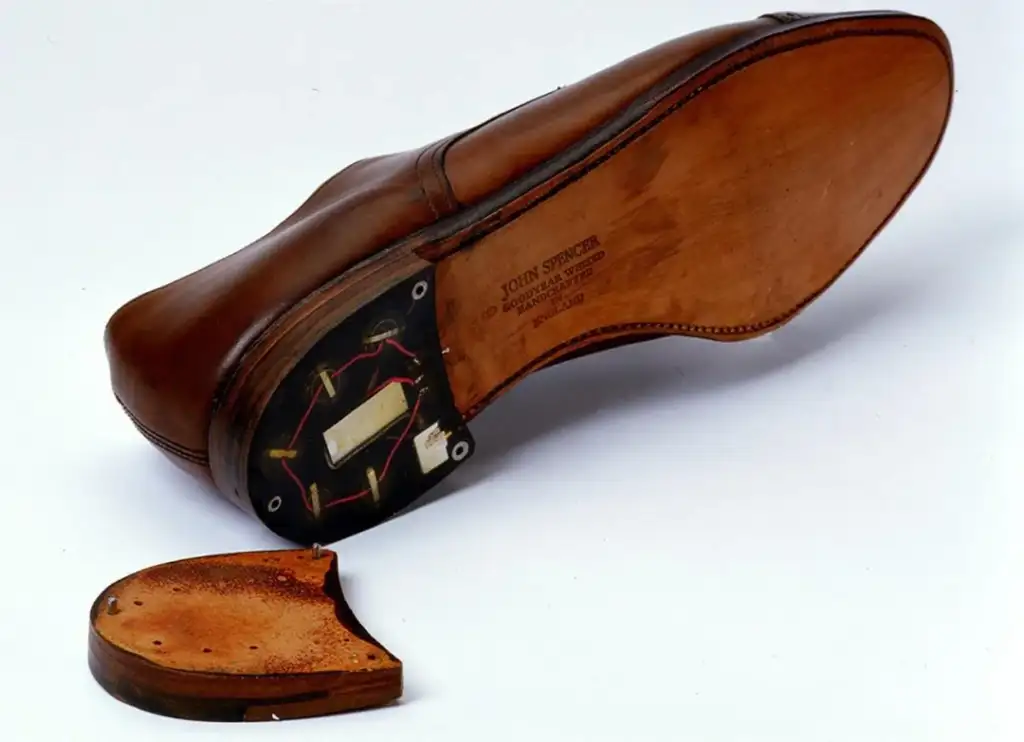 Brown leather shoe with the sole partly removed, revealing a hidden compartment containing wiring and a device. The inner heel section is detached and placed beside the shoe.