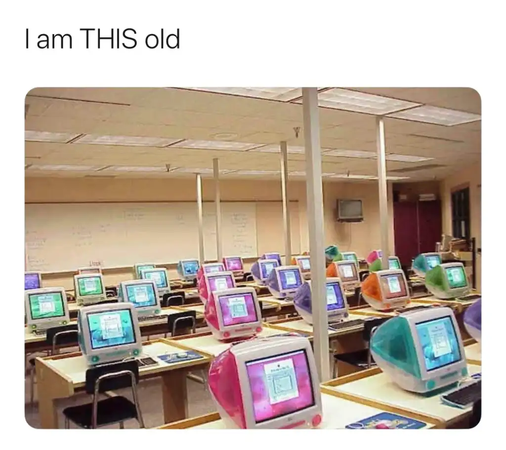 A classroom filled with colorful, vintage iMac G3 computers on desks; colors include pink, blue, orange, and green. The caption above reads "I am THIS old," indicating nostalgia for the era these computers were popular.