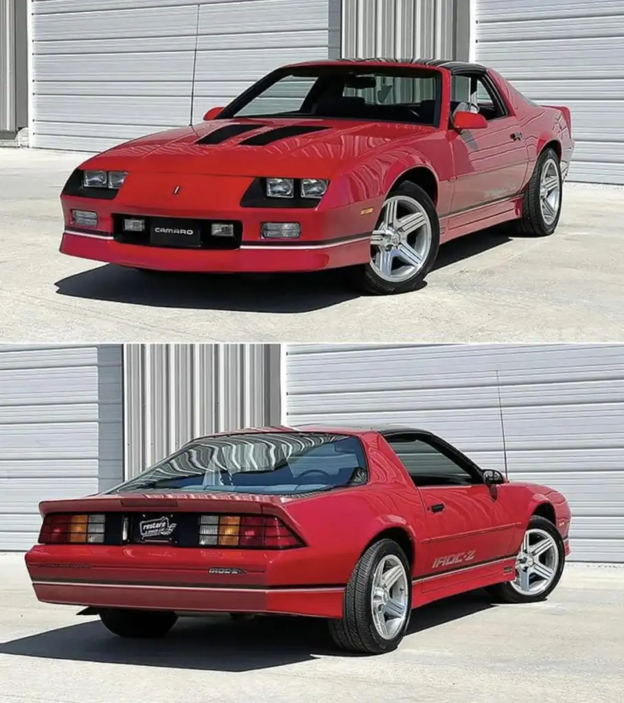 Red Chevrolet Camaro IROC-Z parked in front of a light gray garage. The car features a sleek, sporty design with T-top panels, five-spoke alloy wheels, and distinct IROC-Z decals along the sides and back.