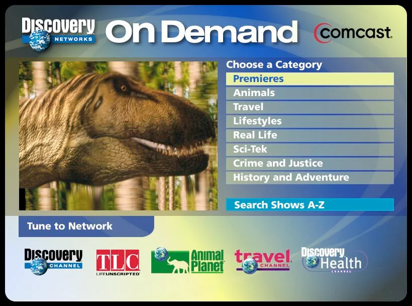 Discovery Networks On Demand menu with a dinosaur image on the left. Categories listed: Premieres, Animals, Travel, Lifestyles, Real Life, Sci-Tek, Crime and Justice, History and Adventure. Network logos: Discovery Channel, TLC, Animal Planet, Travel, Discovery Health.