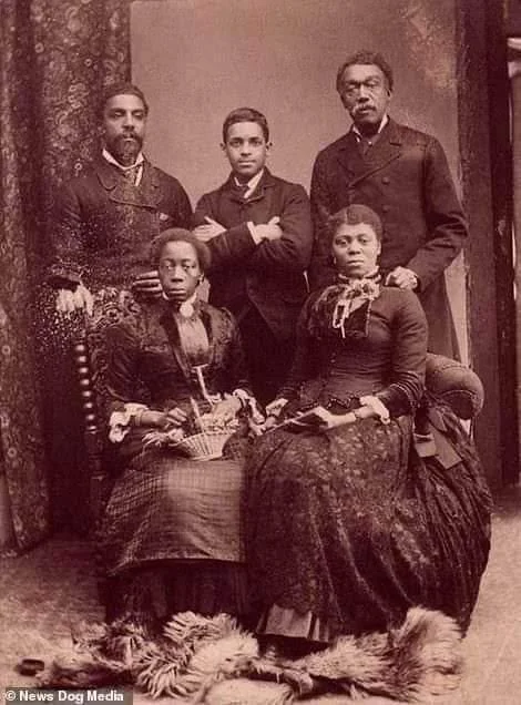 A sepia-toned portrait of five well-dressed individuals from the 19th century. Two women sit in front, wearing long dresses, while three men stand behind them, sporting suits with formal collars. A fur rug lies on the floor in front of them.