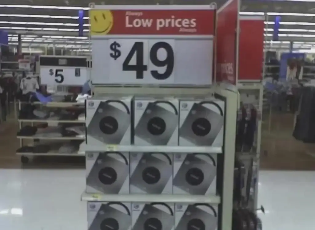 Store display showing shelves packed with boxed headphones priced at $49. A sign above reads "Always Low prices Always" alongside a yellow smiley face. Clothing items priced at $5 are visible in the background.