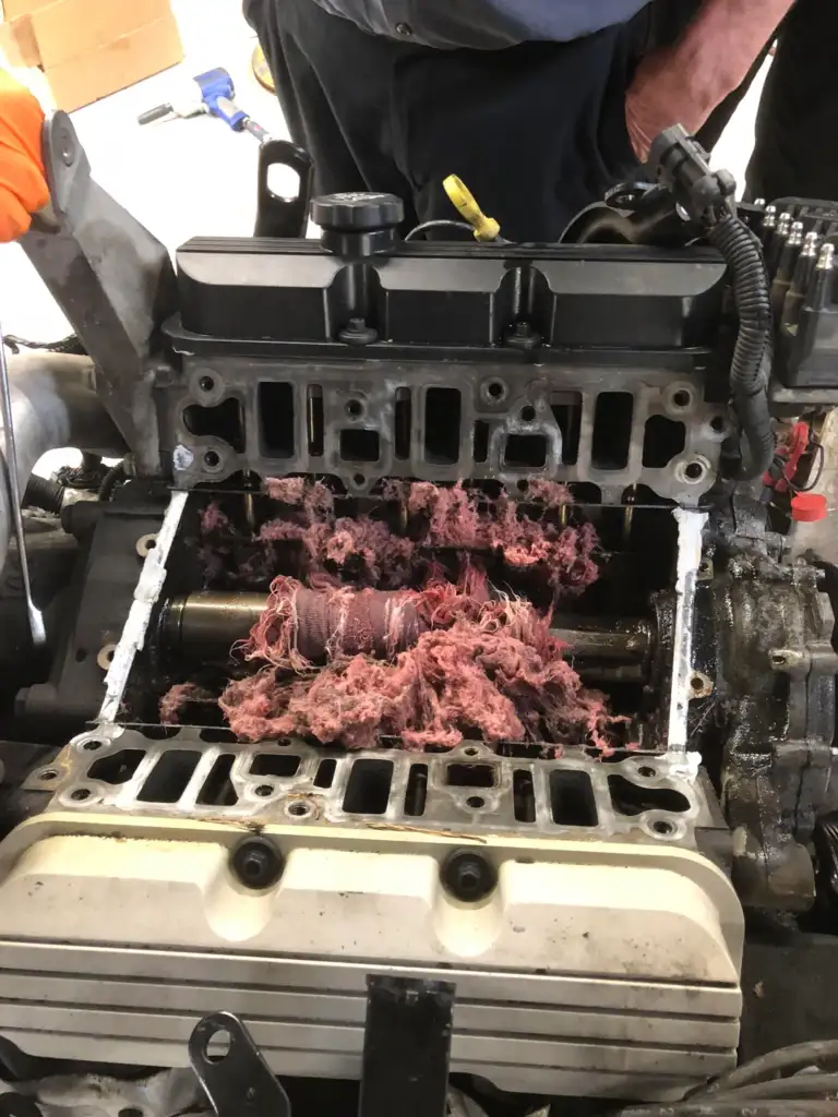 Open car engine revealing internal components tangled with shredded pink fabric, likely causing a malfunction. The image shows mechanical parts partially disassembled, emphasizing the unusual presence of fabric inside the engine.