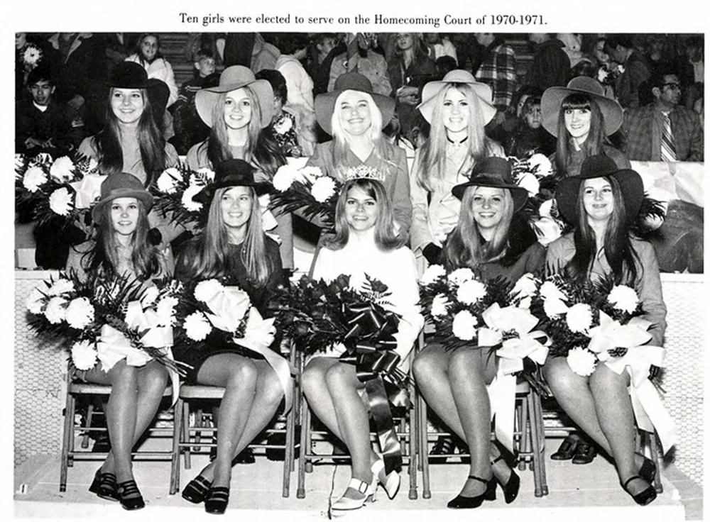 A black and white photo of ten women sitting in two rows, dressed in formal wear with wide-brimmed hats, holding bouquets. A sign above reads "Ten girls were elected to serve on the Homecoming Court of 1970-1971." A crowd is visible in the background.