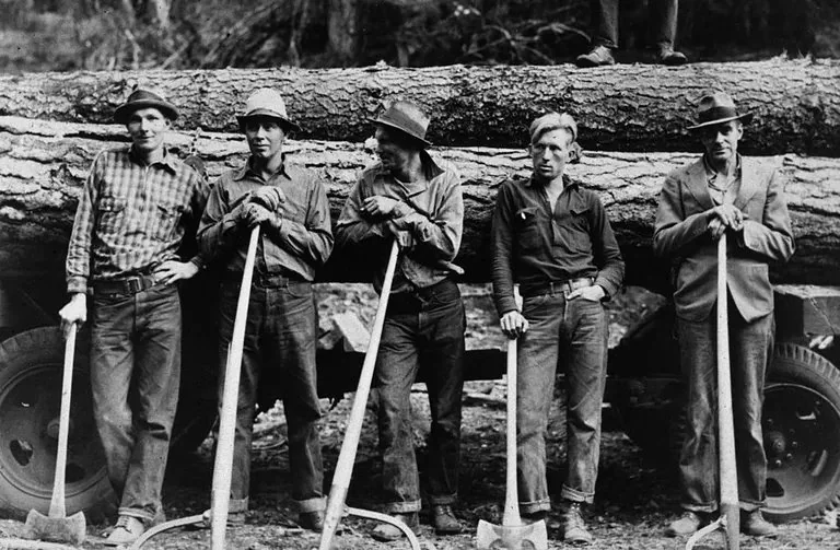 Five loggers stand side by side, leaning on axes in front of a large fallen tree on a truck. They wear hats and work clothes, set in a forested area. The image is in black and white, evoking a historical or vintage feel.