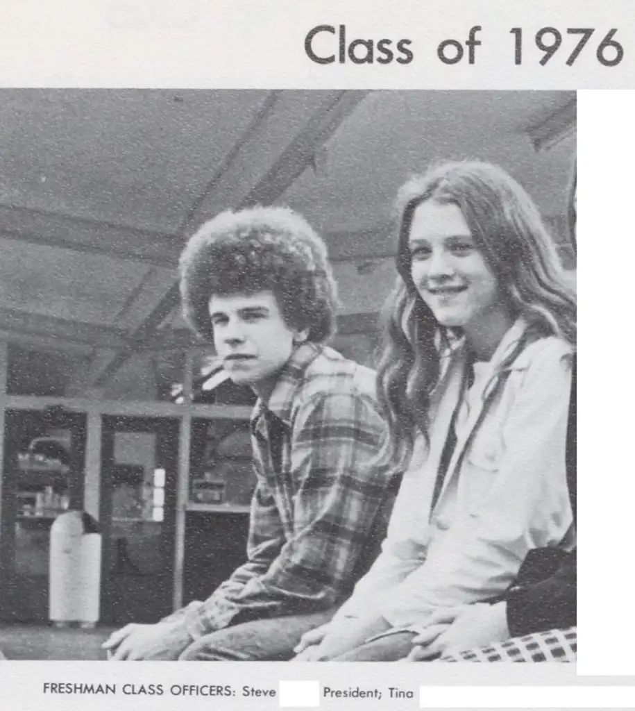 Black and white photo of two young people sitting. The person on the left has curly hair and wears a plaid shirt, with a cigarette in their mouth. The person on the right has long hair and wears a jacket. Text reads "Class of 1976" and "Freshman Class Officers: Steve, President; Tina.