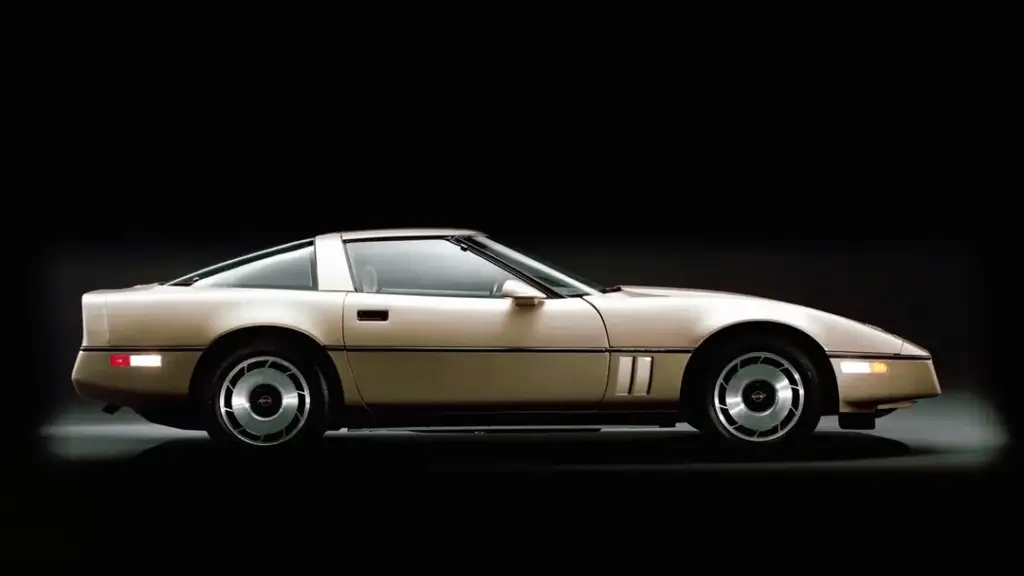 A vintage beige sports car with a sleek, aerodynamic design viewed from the side against a dark background. The car features a targa top and shiny circular hubcaps.