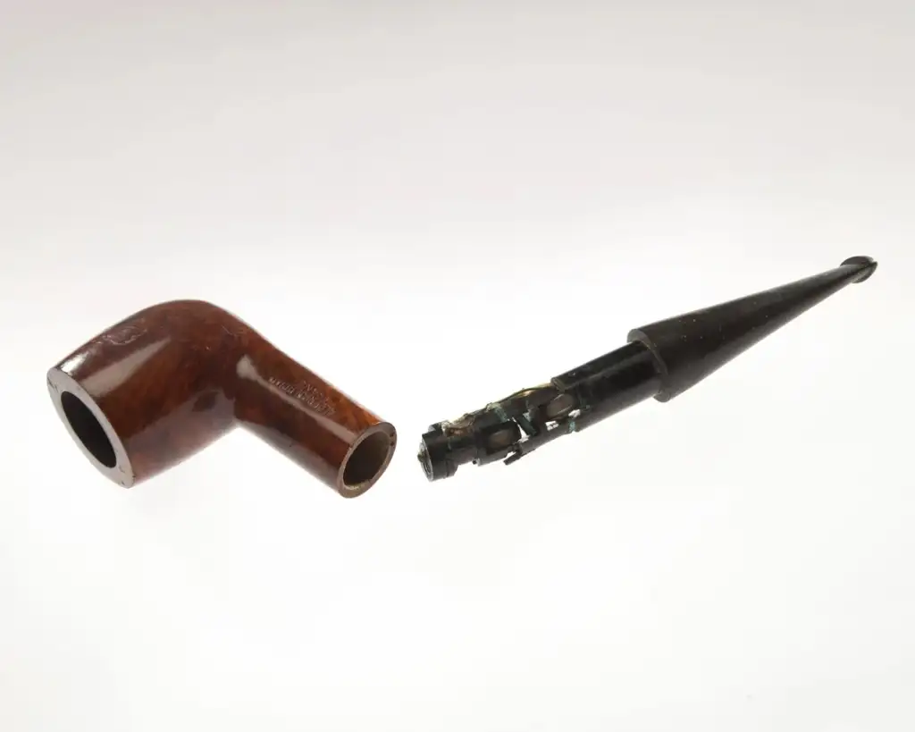 A brown wooden smoking pipe is shown with its mouthpiece detached. The interior reveals a complex mechanical structure, partially visible through the opening. The background is a plain white surface.