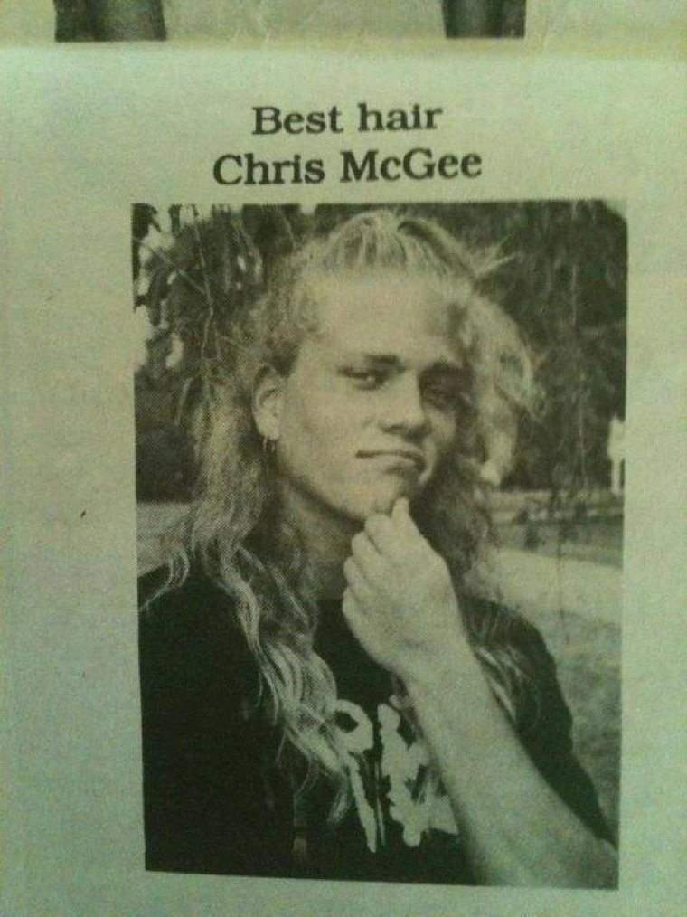 A black and white photo of a person with long, flowing hair, touching their chin and looking at the camera with a slight smile. The text above reads "Best hair Chris McGee." The background is outdoors with some trees visible.