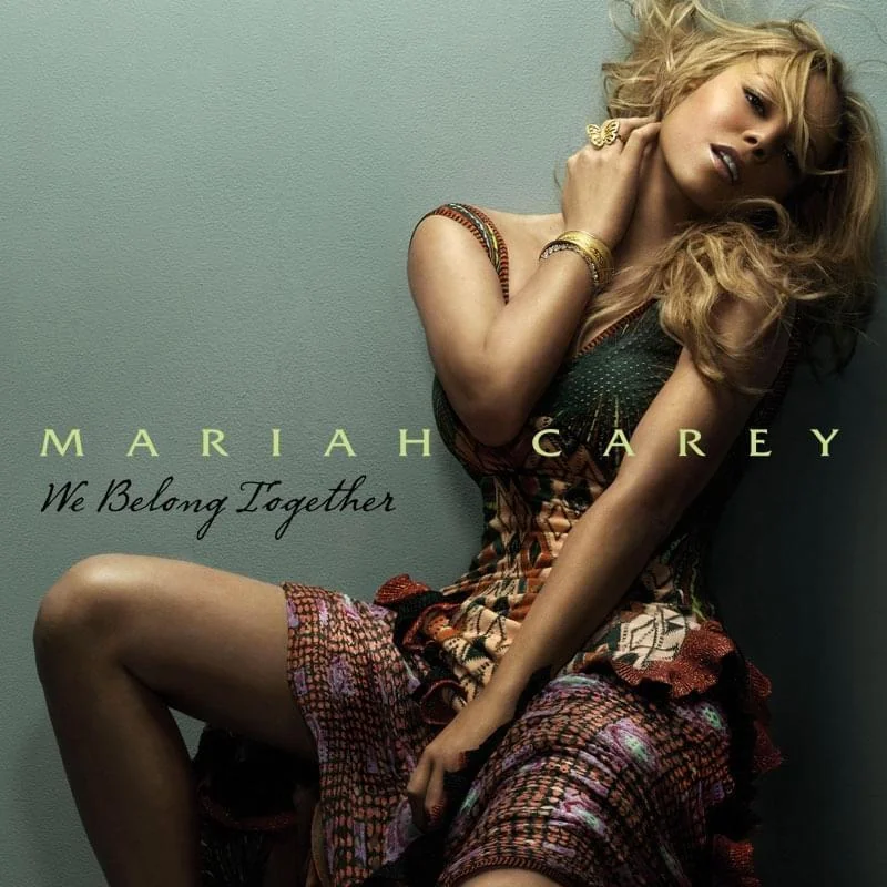 A woman with long, wavy blonde hair poses in a colorful, strapless dress against a neutral background. The text reads "MARIAH CAREY" and "We Belong Together" in elegant font.