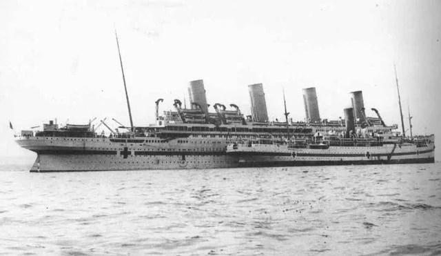 Black and white image of a large ship with four tall funnels on the water. The ship features a cross symbol on its side, indicating its use as a hospital ship. The ocean appears calm under overcast skies.