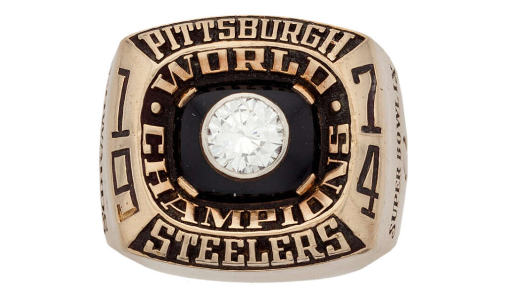 A gold ring with a large central diamond. The surrounding text reads "Pittsburgh World Champions Steelers," with additional details on the sides, including "Super Bowl IX.