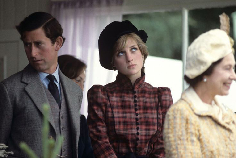 A man in a suit stands next to a woman in a plaid dress and black hat, who is looking upward with an expression of exasperation. Another woman in a light-colored outfit and hat stands in front, smiling.