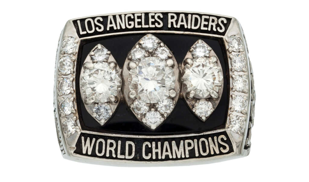 A ring featuring three large, oval-shaped diamonds set on a black background, surrounded by smaller diamonds. The ring is inscribed with "Los Angeles Raiders" at the top and "World Champions" at the bottom.