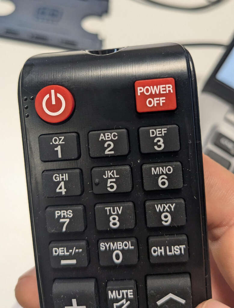 Close-up of a black remote control with a prominent red power button at the top left and another red button labeled "POWER OFF" in the top right corner. Numeric keypad with letters is visible below.