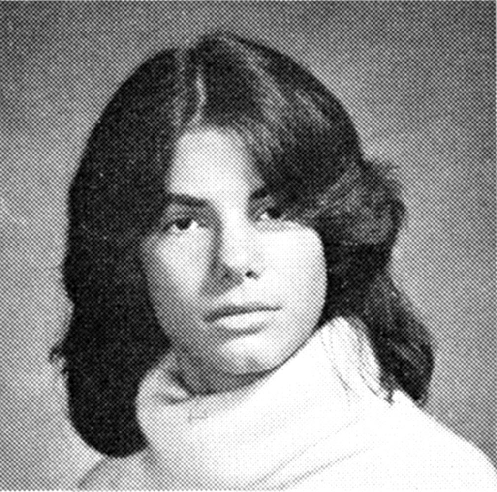 A black and white yearbook photo of a person with long dark hair, wearing a light-colored turtleneck sweater, looking directly at the camera. The background is plain and the image has a vintage appearance.