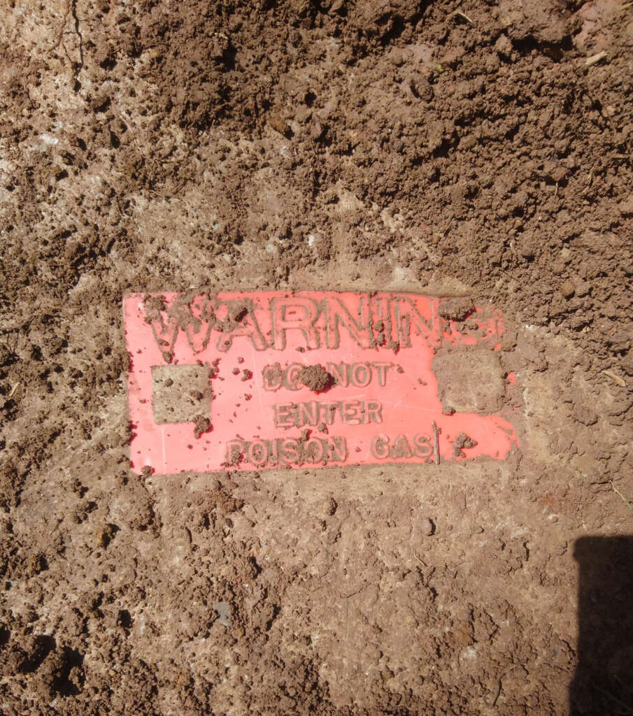 A red warning sign partially buried in dirt reads "WARNING: DO NOT ENTER POISON GAS.