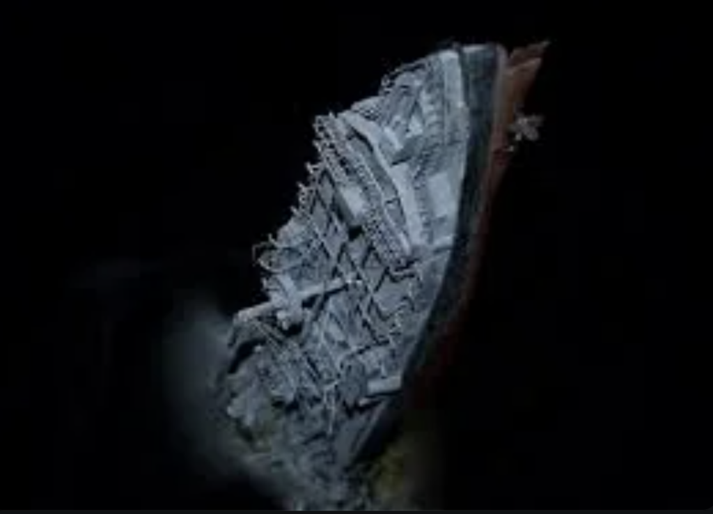 Underwater view of a sunken shipwreck lying on its side in darkness, partially illuminated to reveal its structure. The wreck's skeletal remains are encrusted, indicating long-term submersion.