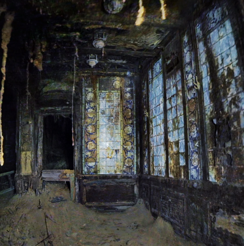 A dimly lit, abandoned room with stained glass windows depicting intricate patterns. The walls and floor are covered in dust and debris, creating an eerie atmosphere. The light filtering through the windows casts blue and yellow hues on the surfaces.