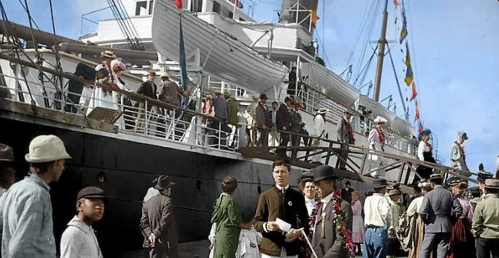 A bustling scene with people boarding or disembarking from a large ship docked at a port. Passengers and crew, dressed in early 20th-century attire, are visible on the deck and pier. The ship's lifeboats and flags are also seen.