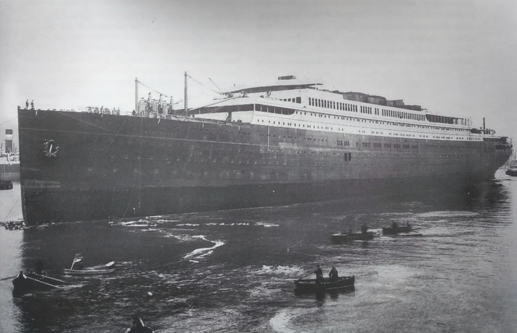 A large, early 20th-century ocean liner with multiple decks, docked in a harbor. Small rowboats with people surround the ship in the foreground. The image is in black and white, indicating it's a historic photograph.