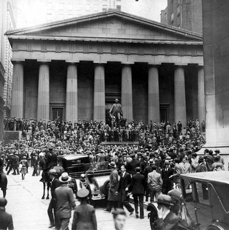 Crowd gathered outside the Federal Hall National Memorial in New York City during the Wall Street Crash of 1929. The scene includes a large group of people, vintage cars, and the building's prominent columns in the background.