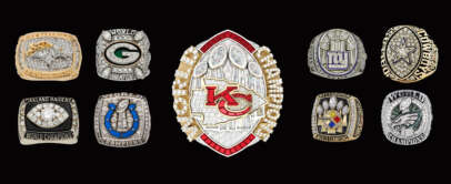 A collection of American football championship rings displayed against a black background. The centerpiece is a Kansas City Chiefs ring, surrounded by rings from various other teams, including the Packers, Raiders, Colts, Giants, Cowboys, Steelers, and Eagles.