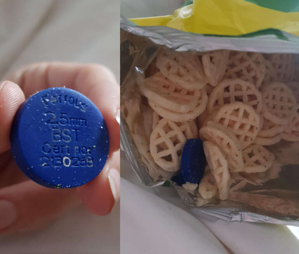 Close-up of a hand holding a blue plastic disk with "25mm BST Cert no. 213023" inscribed, next to an open bag of snack chips resembling small lattices. The disk is partially inside the bag along with the snacks.