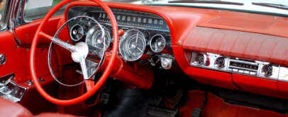 Interior of a vintage car featuring a red leather dashboard and steering wheel. The dashboard includes classic analog gauges and a radio. The car’s upholstery and carpet are also in matching red.