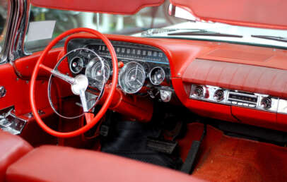 Interior of a vintage car featuring a red leather dashboard and steering wheel. The dashboard includes classic analog gauges and a radio. The car’s upholstery and carpet are also in matching red.