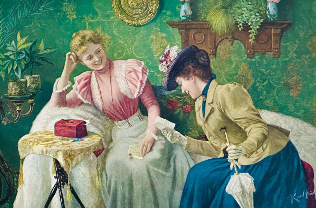 Two women in Victorian attire sit on a sofa in an ornate room with floral wallpaper. One, in a pink dress, smiles while the other, in a blue dress and hat, shows her a letter. A small table with a red box is beside them.