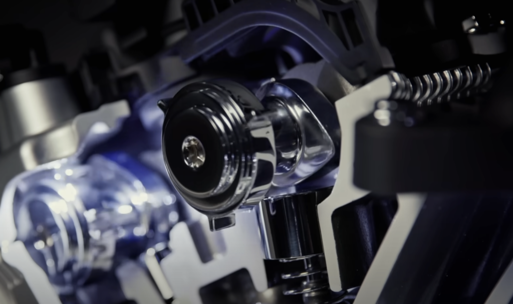 Close-up of a metallic engine component with a shiny, reflective surface. Springs and other mechanical parts are visible, showcasing intricate details and engineering. The lighting highlights the polished metal, emphasizing its texture and precision.