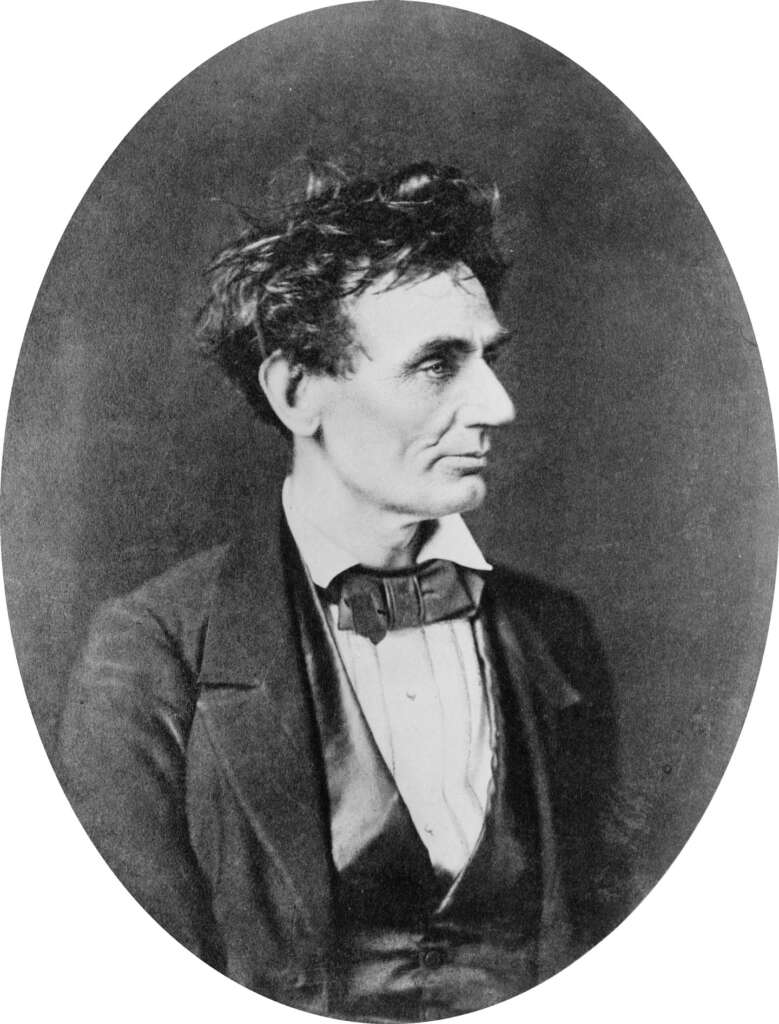 Black and white portrait of a man in profile, with unruly hair and wearing a suit with a bow tie. The image has an oval frame, giving it a classic, vintage appearance.