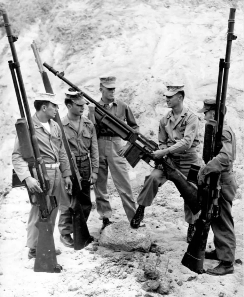 Five soldiers in uniform stand outdoors holding large anti-tank rifles, with two of them helping to hold a single rifle in the center. The scene appears to be set on a sandy or rocky terrain.