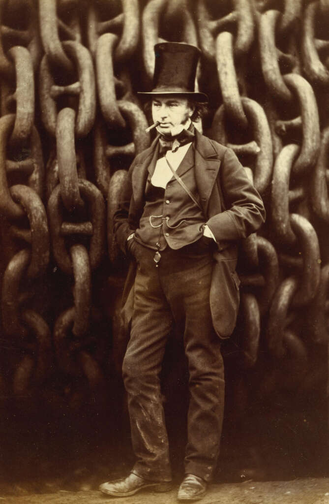 A bearded man in a top hat and suit stands confidently with hands in pockets in front of large, heavy chains. The background features a close-up view of interlocking chain links. The sepia tone gives the image a vintage appearance.