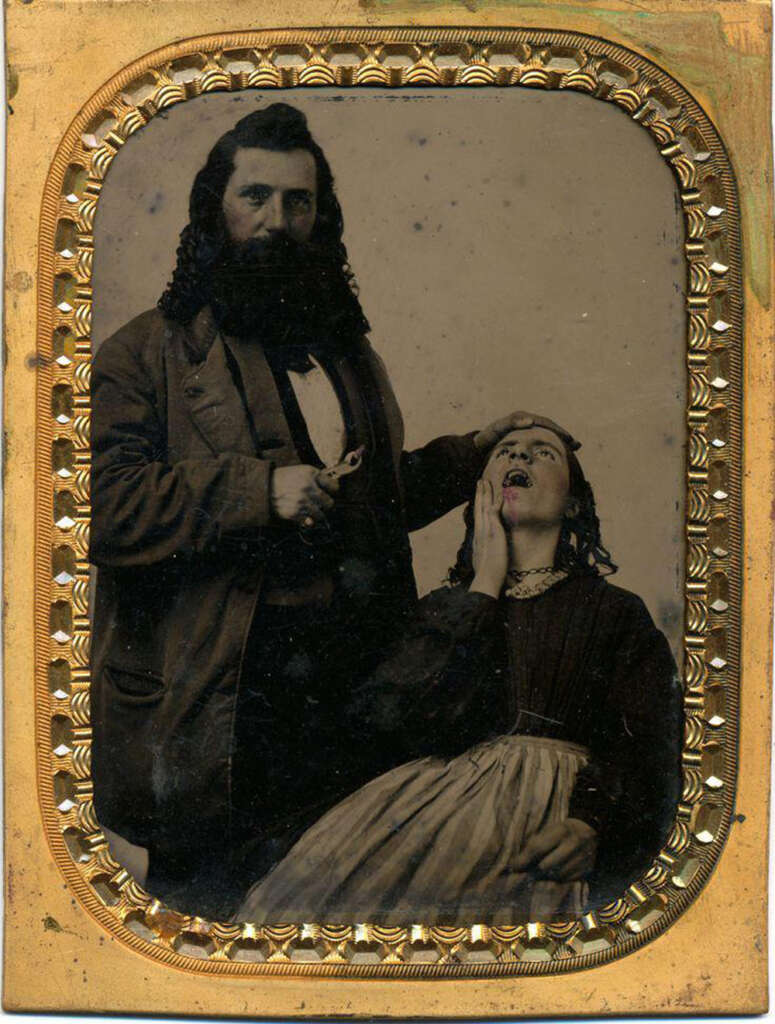 A historical photograph shows a man with a beard and curly hair standing, dressed in a suit. He holds a dental tool to a seated woman's open mouth. She wears a Victorian dress, appearing distressed. The image is framed with an ornate, gilded border.