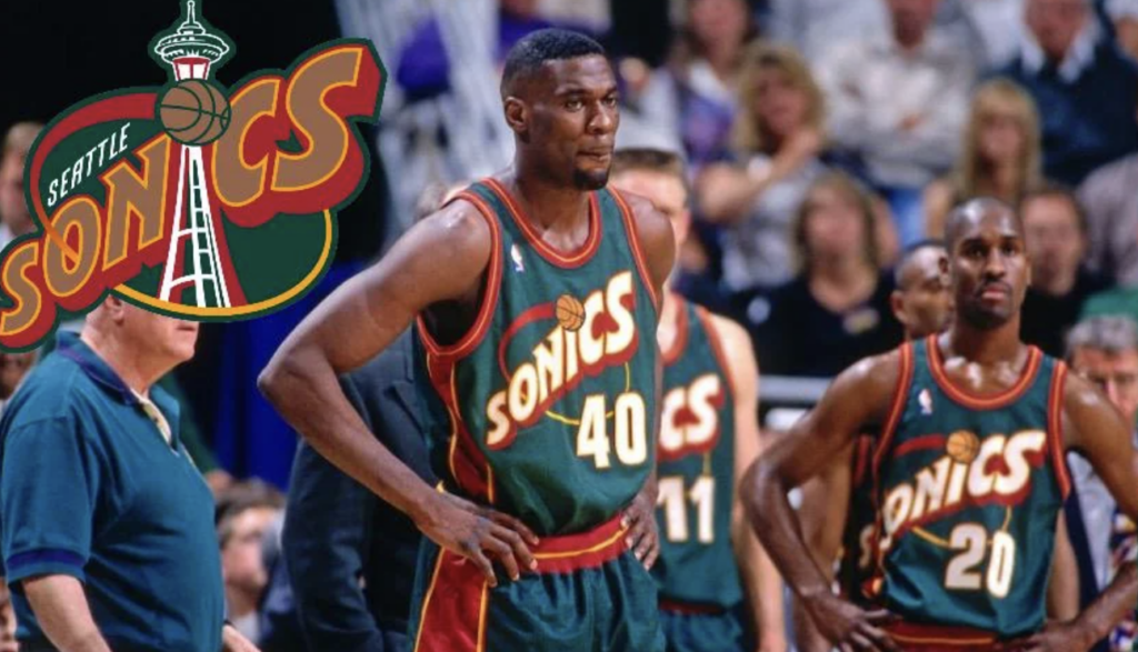 Basketball players in Seattle SuperSonics uniforms stand on a court. A large team logo is displayed to the left. The scene includes an audience in the background.