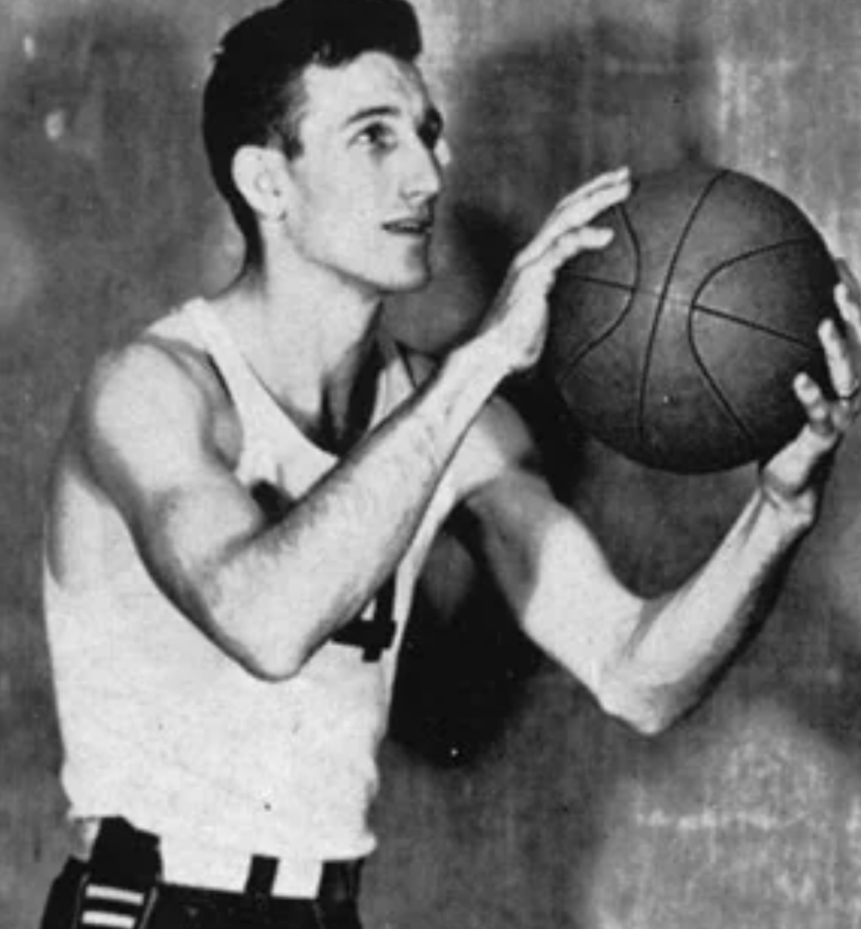 A vintage black-and-white photo of a basketball player preparing to shoot. The player is wearing a sleeveless jersey with the number 14 and holds the ball with both hands near his chest, looking focused. The background is plain.