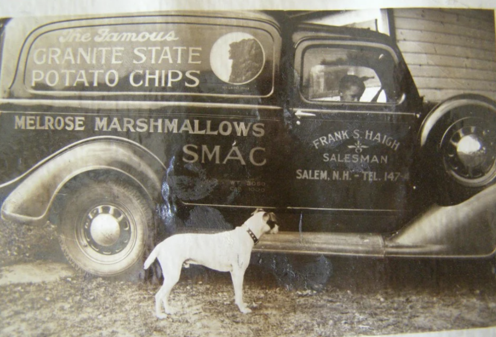 A vintage black and white photo shows an old delivery van with "Granite State Potato Chips" and "Melrose Marshmallows" painted on it. A dog stands beside the van, and a driver is visible inside.