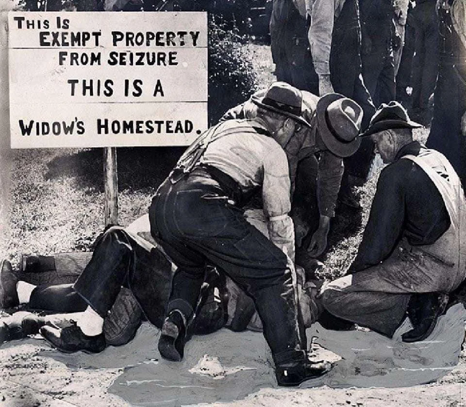 A group of men in overalls and hats crouch around a person lying on the ground. A sign nearby reads, "This is exempt property from seizure. This is a widow's homestead." The scene appears tense and urgent.