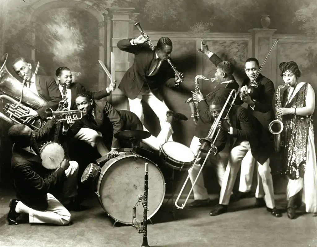 A vintage black and white photo of a lively jazz band. Members energetically play various instruments, including a tuba, trumpet, drums, saxophone, and clarinet. The band is captured in dynamic poses, creating a sense of motion and excitement.