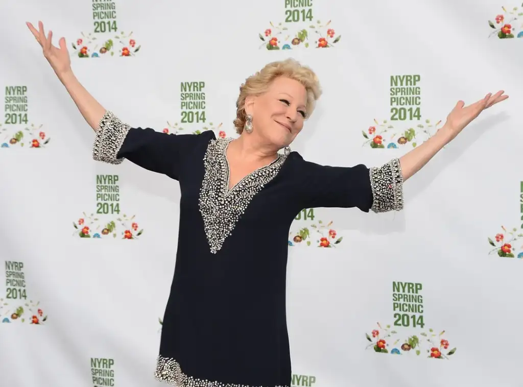 Person in a navy dress with white accents stands embracingly in front of a backdrop with "NYRP Spring Picnic 2014" logos.