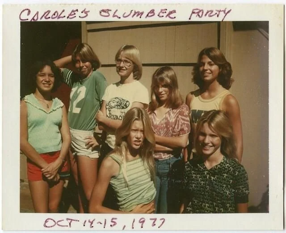 A vintage photo from "Carole's Slumber Party" dated October 14-15, 1977, shows a group of seven smiling people standing outdoors. They're casually dressed in 1970s fashion, with one person wearing a sports jersey.