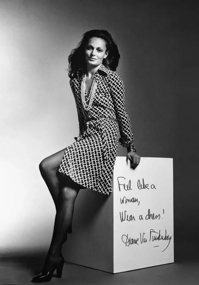 Black and white photo of a woman sitting on a cube. She's wearing a patterned dress and heels. The cube has handwritten text: "Feel like a woman, wear a dress! Diane von Furstenberg.