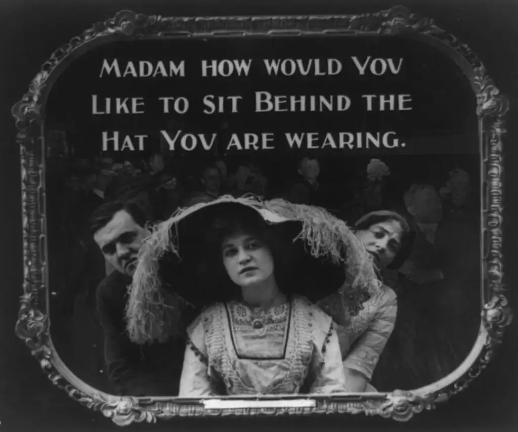 Black and white photo of a woman in a large hat seated in a theater, with two people looking over her shoulders. Text above reads, "Madam, how would you like to sit behind the hat you are wearing.