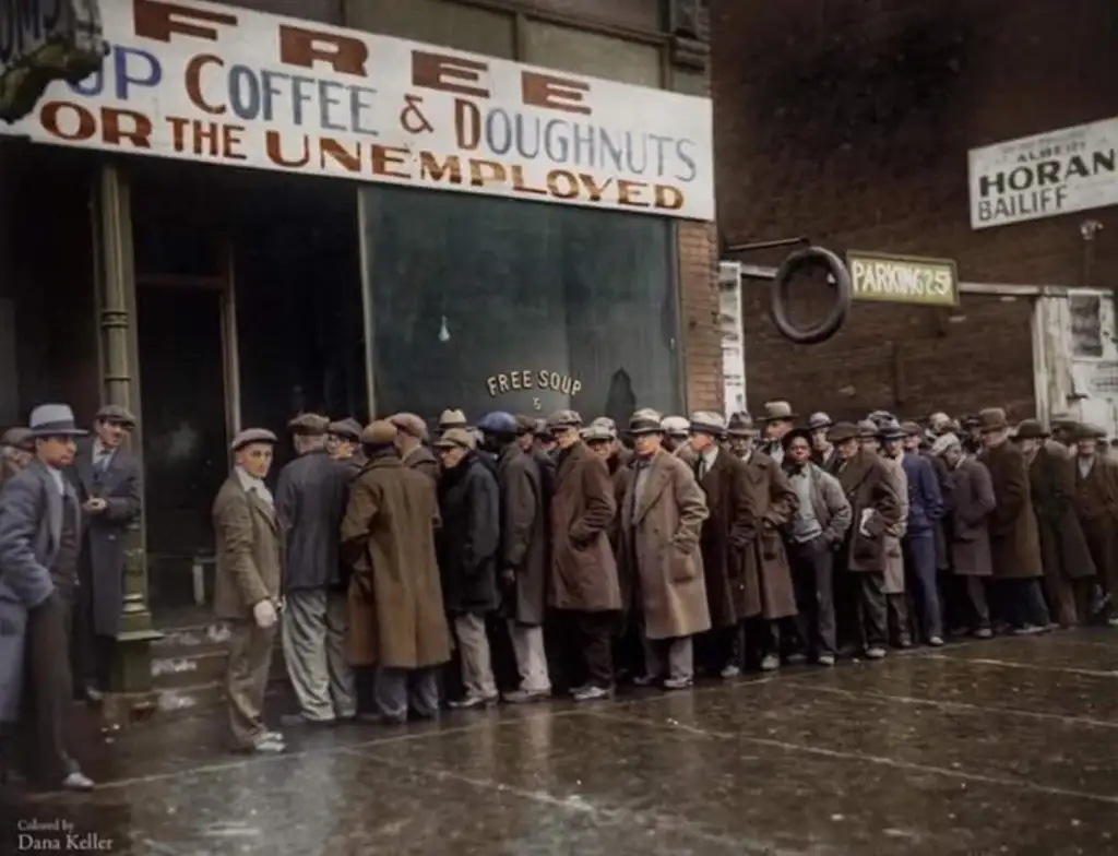 A long line of people in 1930s attire wait outside a building offering free soup, coffee, and doughnuts for the unemployed. The sign above reads "Free Soup Coffee & Doughnuts for the Unemployed." The scene is set on a rainy day.