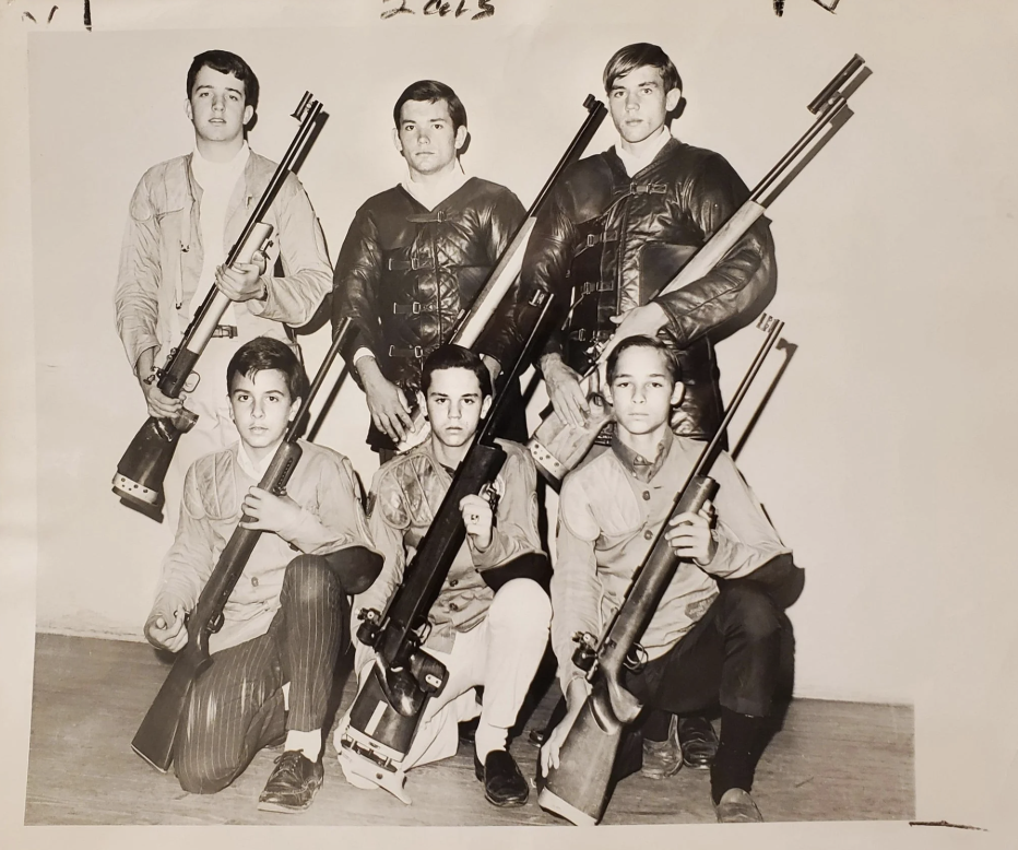 Black and white photo of six young men posing with rifles. Three are standing, wearing jackets, and three are kneeling in front, all holding rifles. They're in a staged, team-like formation, possibly for a shooting competition or club.