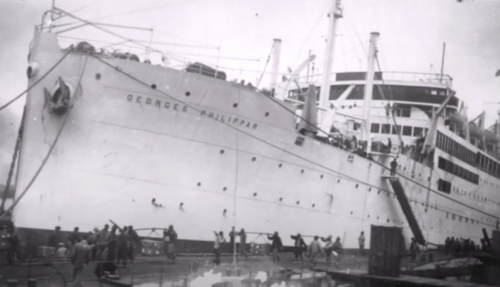 Black and white photo of a large ship named "Georges Philippar" docked at a port. People are seen boarding or disembarking via a gangway. There are many individuals and some activity on the pier, reflecting a bustling scene.